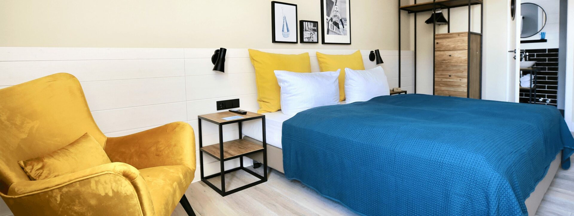 Längliches Foto von einem Hotelzimmer in Heringsdorf mit einem Doppelbett, Garderobe, Nachttischen, Sessel und separatem Bad