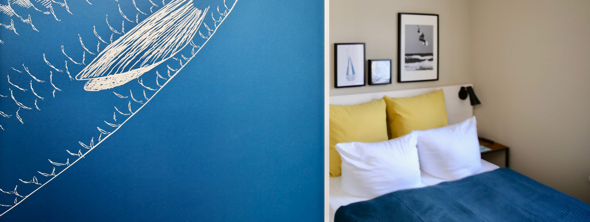 Längliches Foto von einem Hotelzimmer in Heringsdorf, links wird der Blick durch eine blaue Wand mit weißem Fischmotiv verdeckt