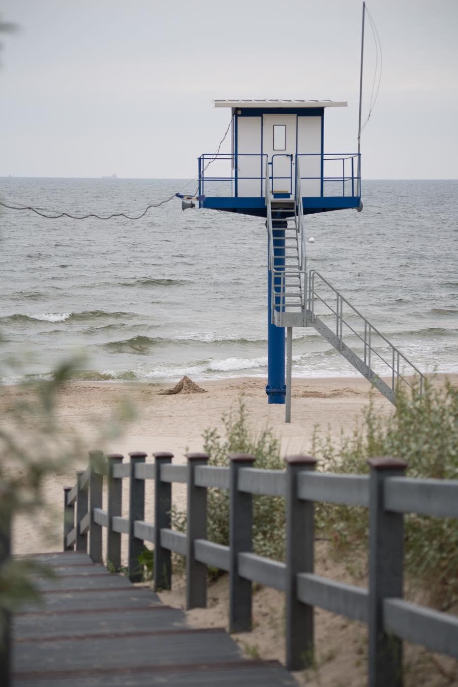 Nahe eines Boutique Hotels auf Usedom führt ein hölzerner Steg zu einem Strand, auf dem ein Rettungsschwimmer-Turm steht