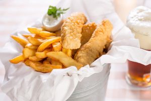 Ein leckeres Fish & Chips Gericht in einem Eimer steht zusammen mit einem Bier auf einem Tisch in einem Hotel in Heringsdorf