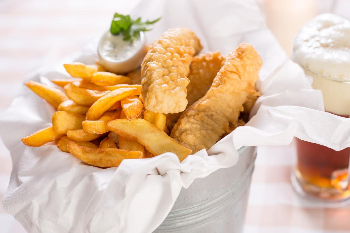 Ein leckeres Fish & Chips Gericht in einem Eimer steht zusammen mit einem Bier auf einem Tisch in einem Hotel in Heringsdorf