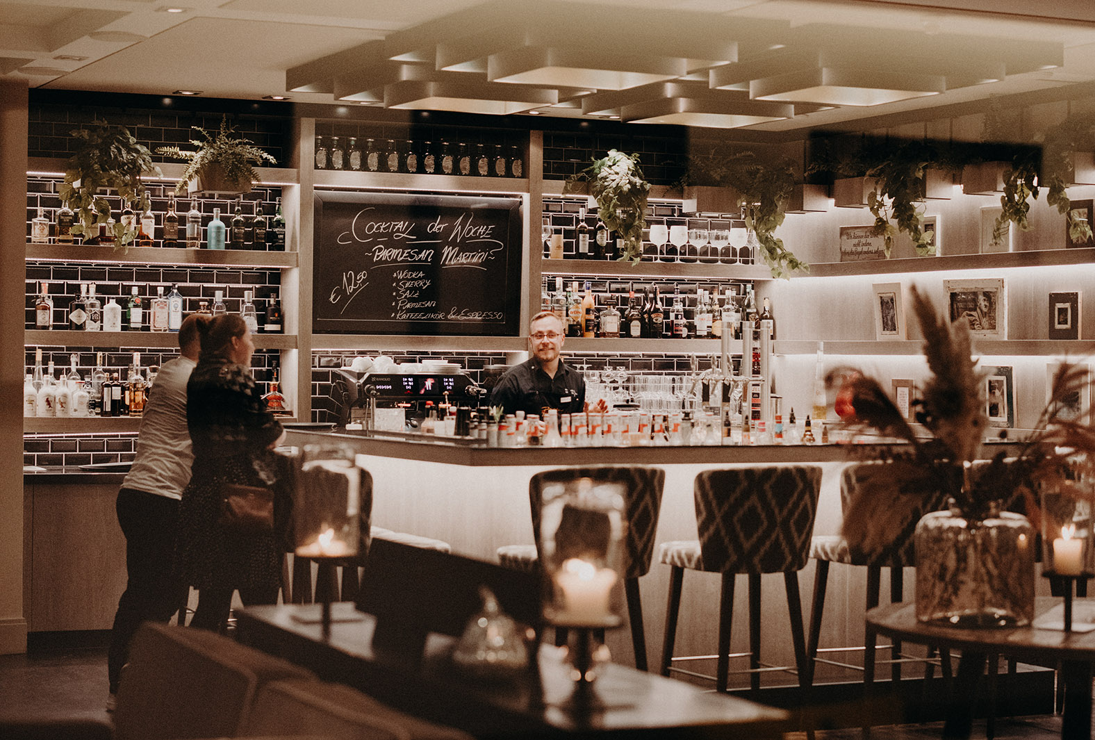 Foto von zwei Gästen und einem Barkeeper, die an einer gut ausgestatteten Bar in einem Hotel mit Frühstück in Heringsdorf stehen