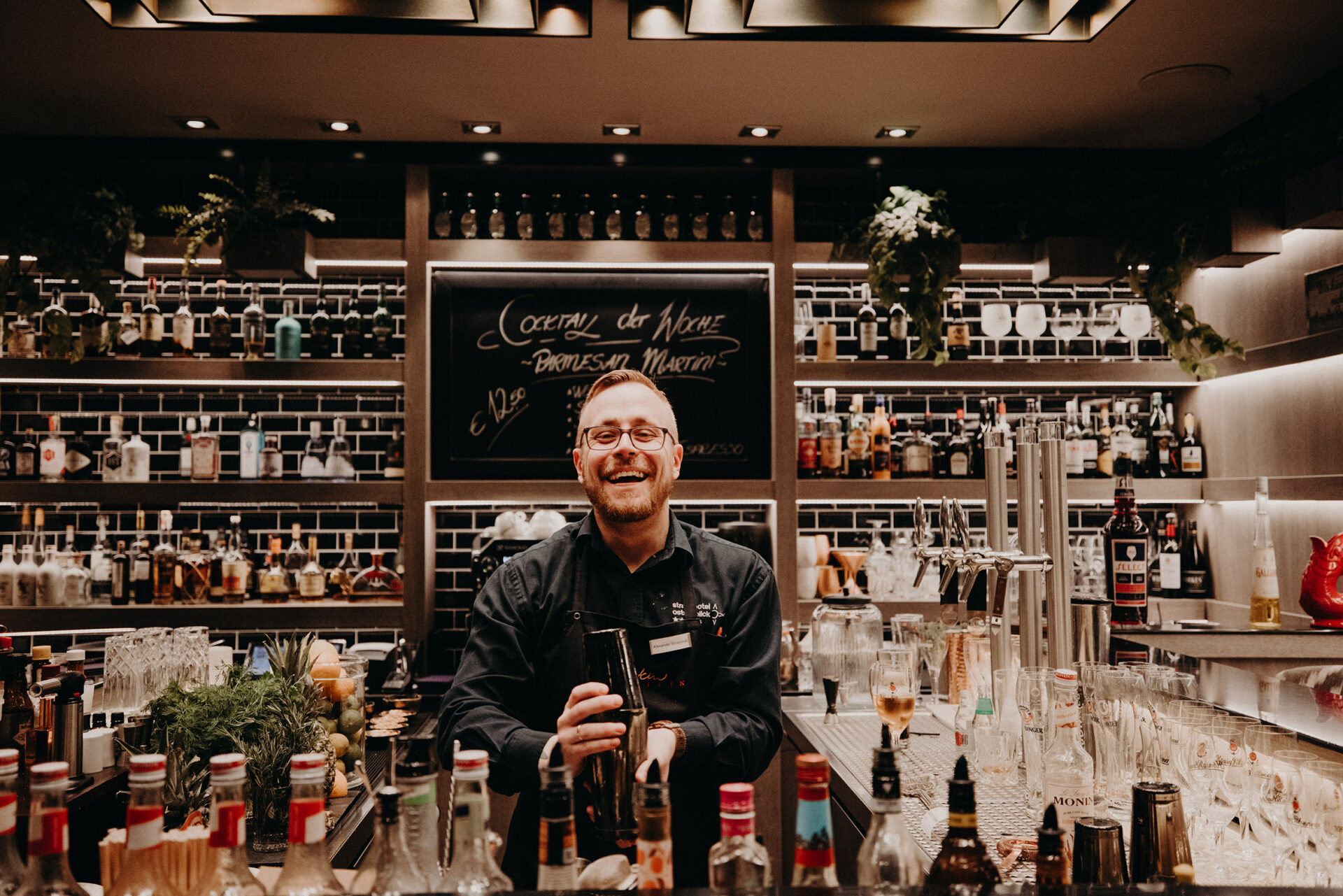 Ein lachender Barkeeper bereitet in einer gut ausgestatteten Bar in einem Hotel Garni in Heringsdorf einen Cocktail zu