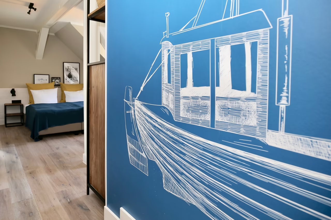 Nahaufnahme einer blauen Wand mit einer weißen Bootszeichnung, im Hintergrund sieht man ein Hotelzimmer in Heringsdorf