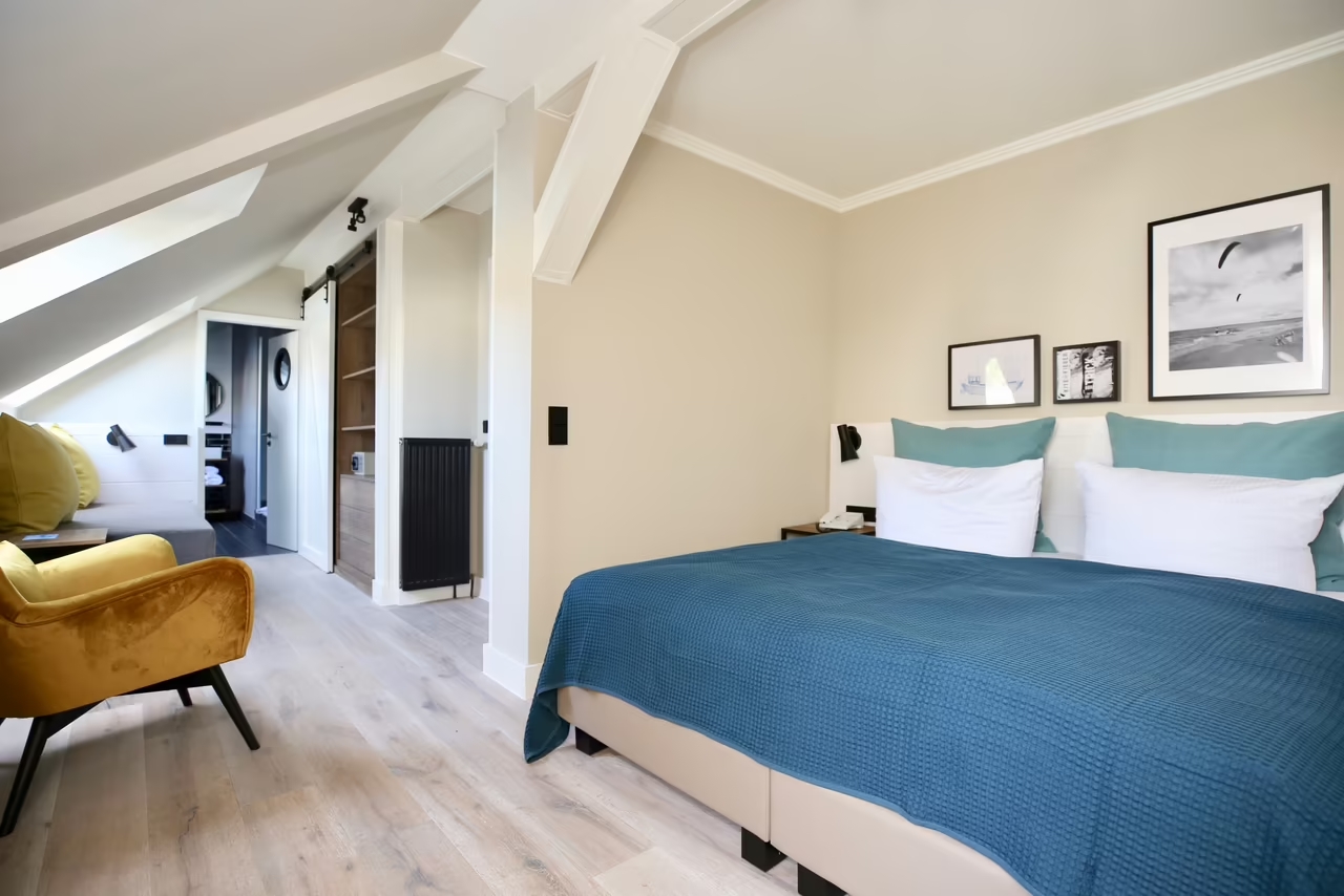 Foto eines geräumigen Hotelzimmers unter einer Dachschräge in Heringsdorf mit Doppelbett, Sitzbereich, Schrank und Badezimmer