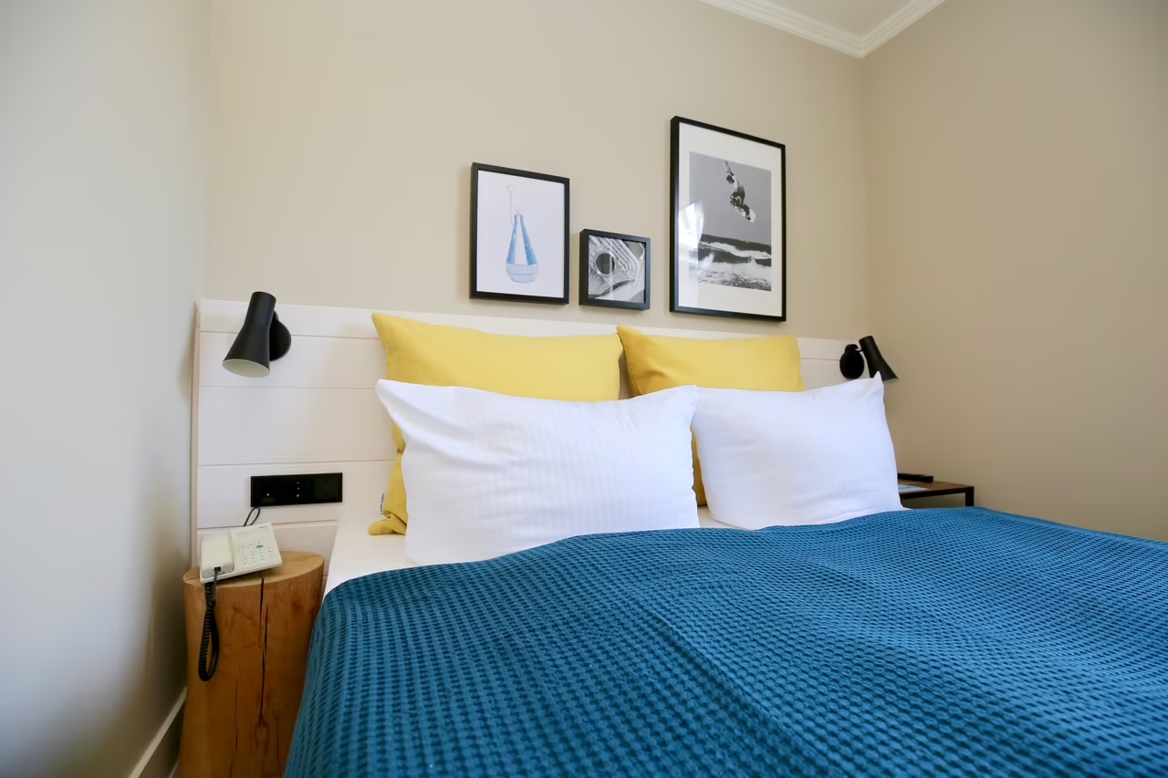 Aufnahme von einem einladenden Doppelbett in einem Hotelzimmer in Heringsdorf, über dem Bett hängen drei maritime Bilder