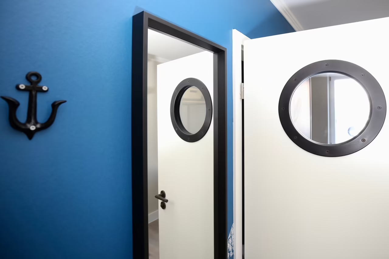 Eine weiß-schwarze Tür mit einem Bullaugen-Fenster und ein Garderobenhaken in Ankerform in einem Hotelzimmer in Heringsdorf