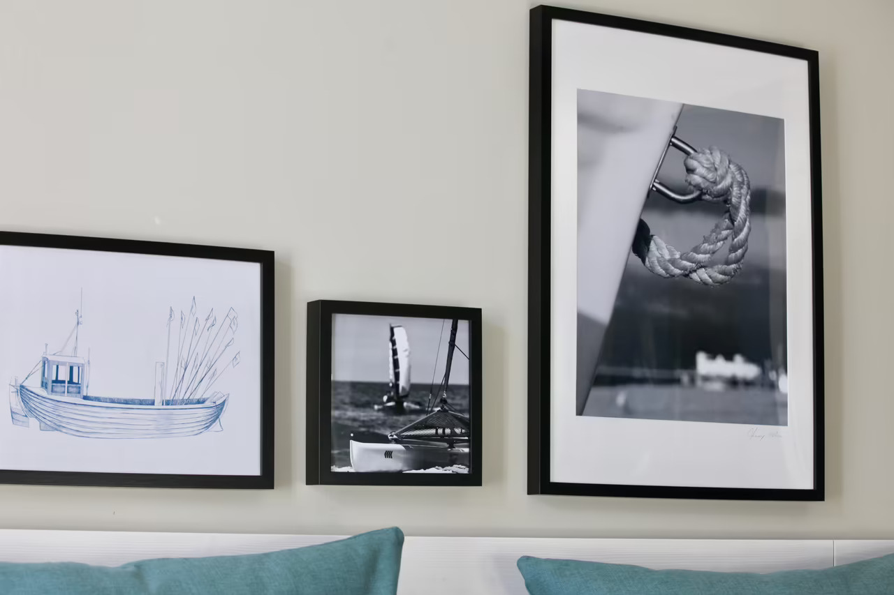 Nahaufnahme von drei eingerahmten Fotos mit maritimen Motiven, die über einem Bett in einem Hotelzimmer in Heringsdorf hängen