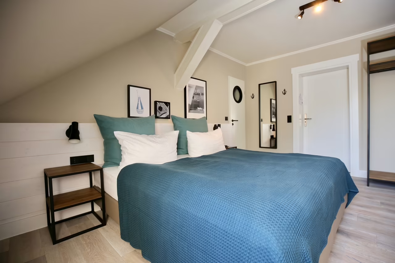 Einladendes Doppelbett mit zwei Nachttischen, blauer Überdecke und vier Kissen in einem Hotelzimmer in Heringsdorf