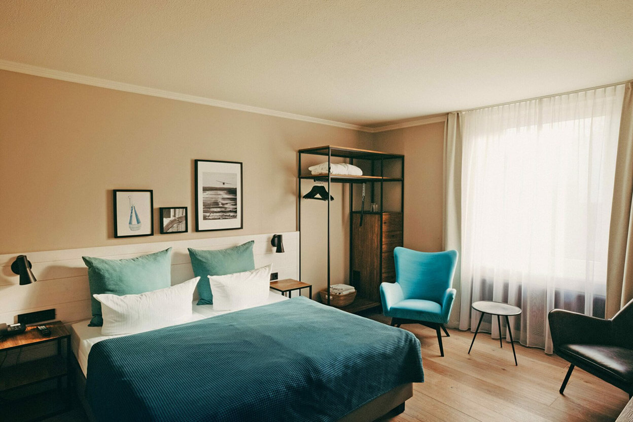In einem einladenden Hotelzimmer in einem Hotel in Heringsdorf steht ein Doppelbett, eine Garderobe sowie zwei Sessel